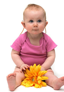 Baby with hearing aids holding a flower